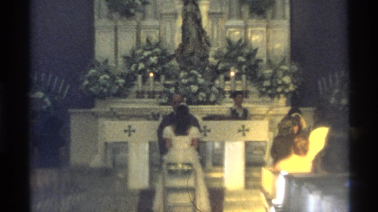 Wedding ceremony continues at a flowered altar inside a church.