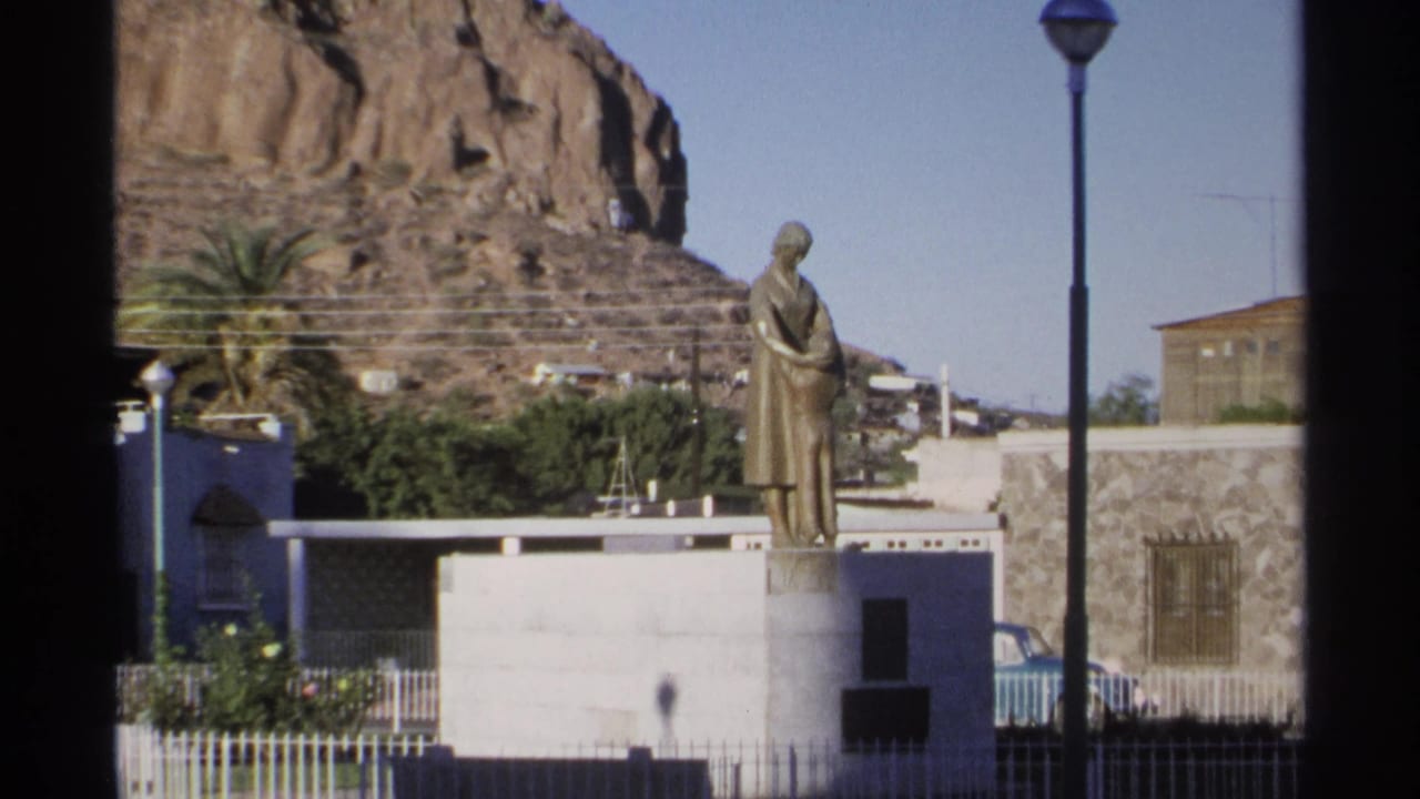 Bronze mother-and-child statue on a white pedestal with a rocky hillside behind it.