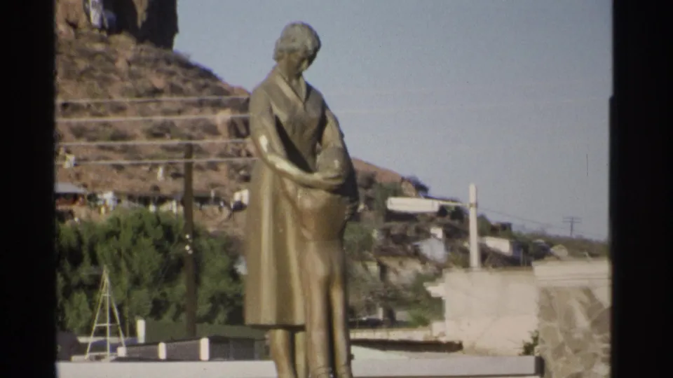 Tight 1975 Guaymas frame of the mother-and-child statue, with rocky hillside, trees, and plaza structures in the background.