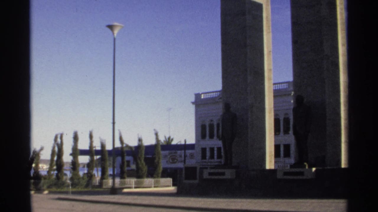 Tall concrete pillars and bronze statues seen through dark foreground framing.