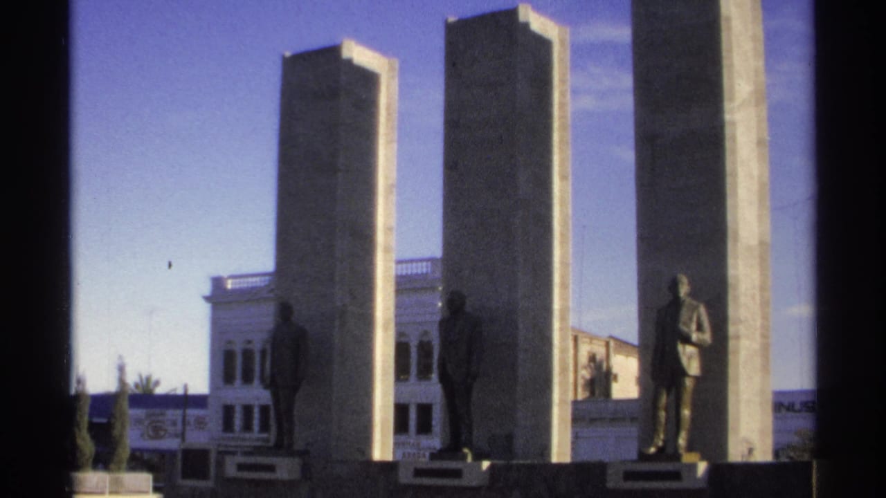 Stone pillars with standing statues in front of a white building.