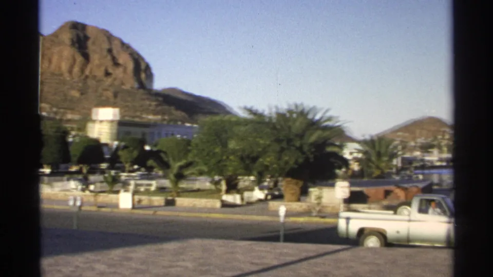 Guaymas, Mexico street scene with palms, vehicles, a rocky hill, and distant waterfront glimpsed through window framing.