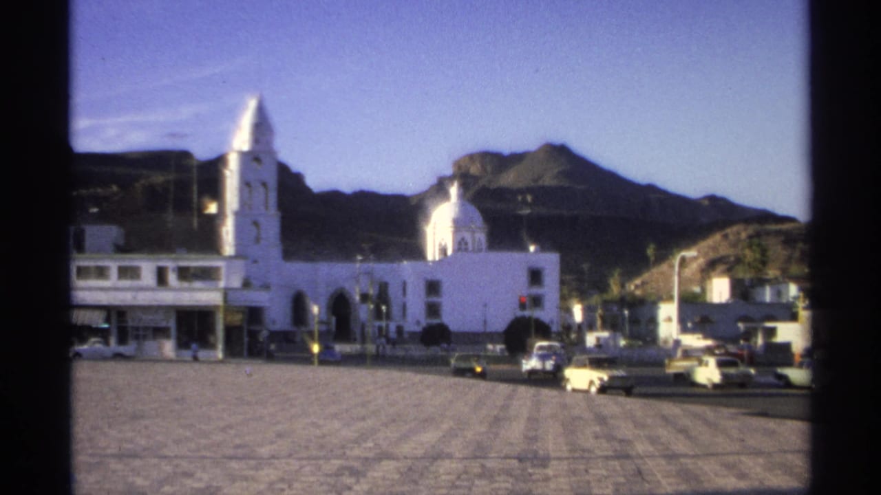 Town square with white church, mountains, and several cars near the curb.