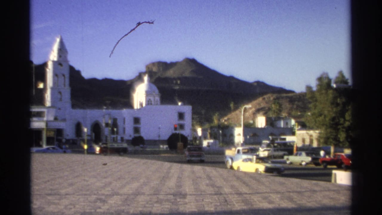 White church and plaza with parked cars and mountains in the background.