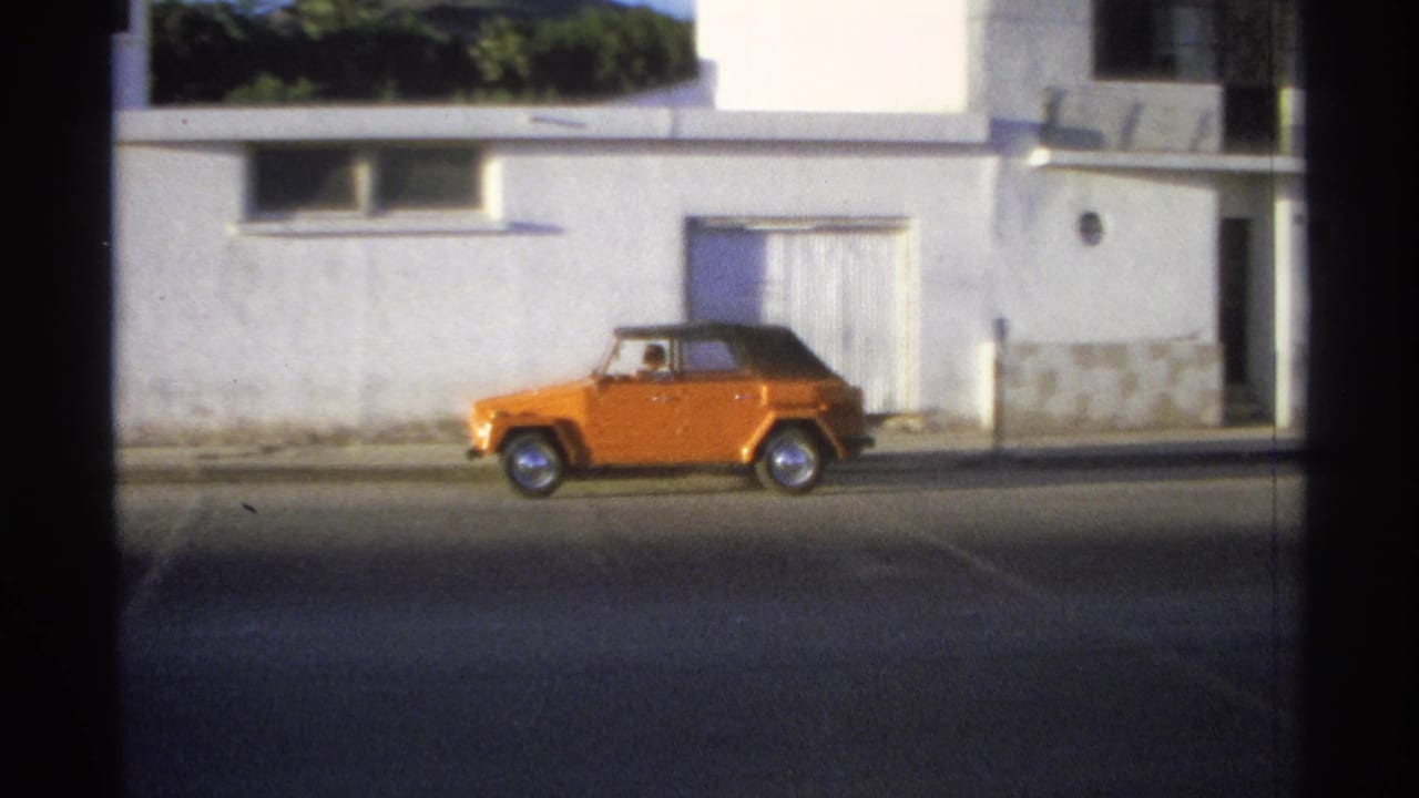 Orange car seen farther along the street beside a white building and curtained opening.