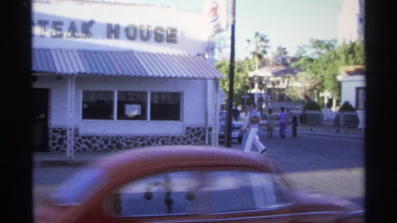 Steakhouse exterior across a street with pedestrians and a passing red car.