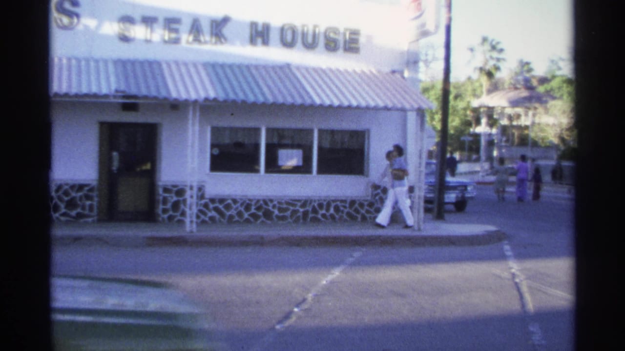 White steakhouse facade with a pedestrian in white pants near the sidewalk.