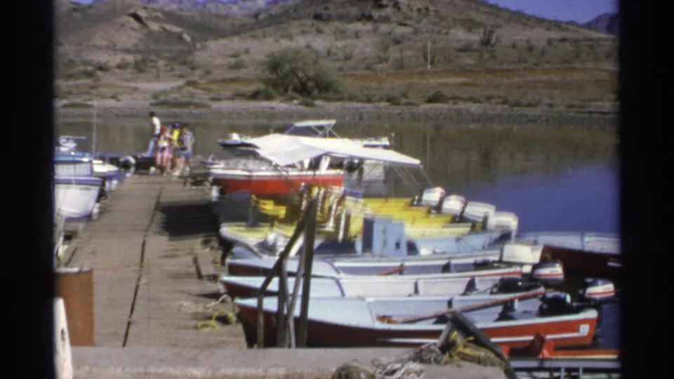 A Guaymas marina dock holds red, yellow, and white boats as people stand near the water in 1975 travel footage.
