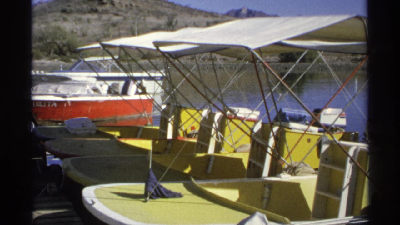 Yellow boats and a red motorboat moored beside a wooden dock with arid hills beyond.