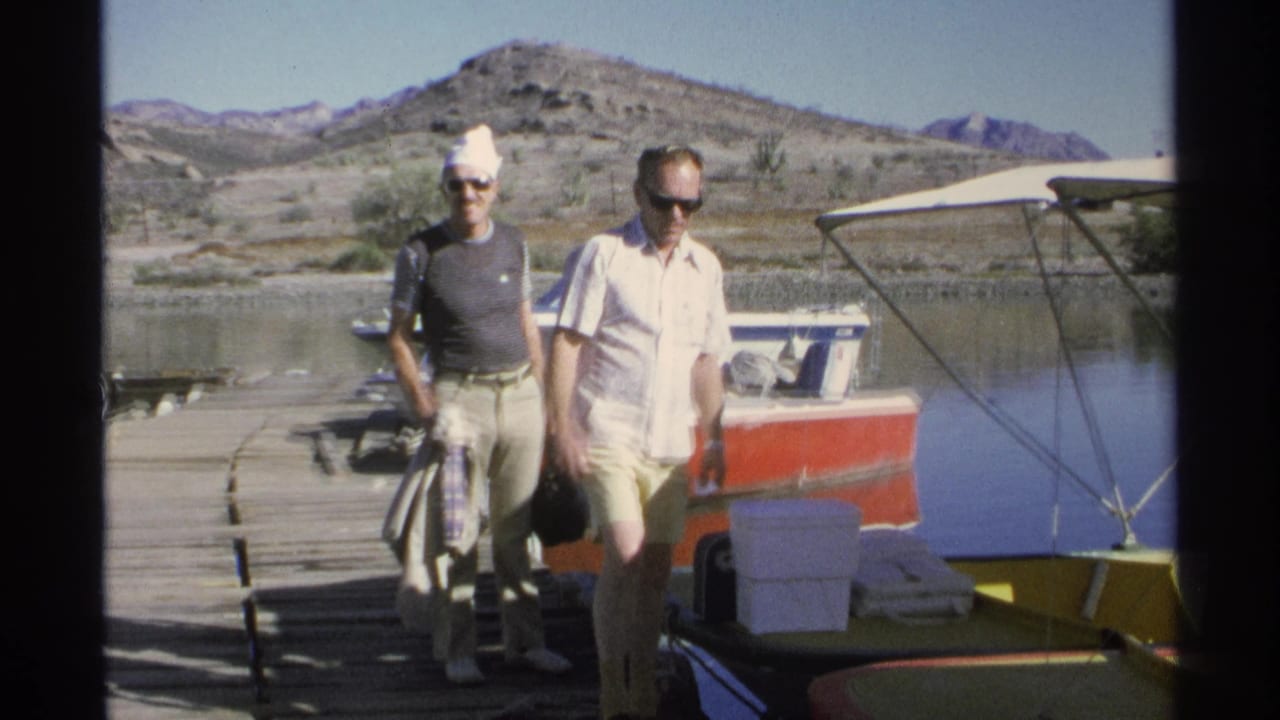 Two adult men walk on a dock beside small boats and fishing gear.