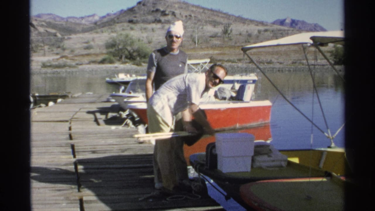 A man bends over fishing gear while another man in sunglasses stands near a boat.