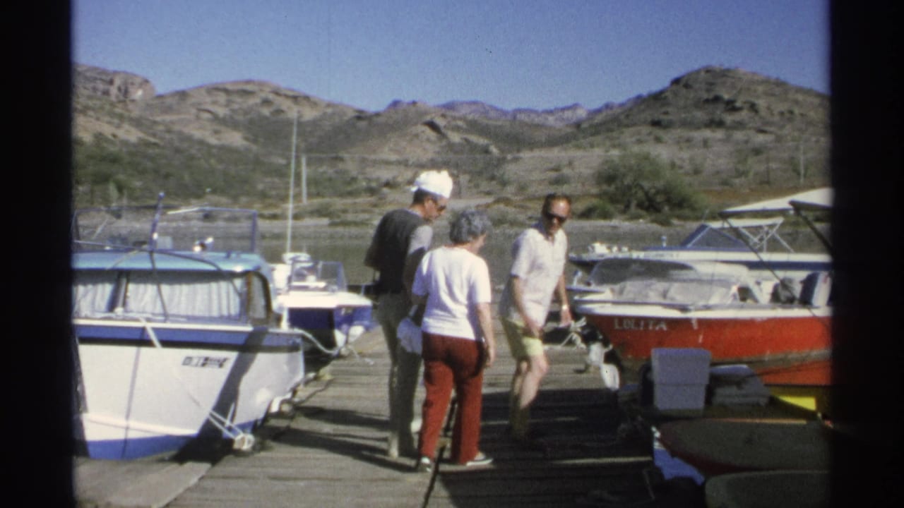 Adults pause on a dock near a red-and-white boat and other moored vessels.