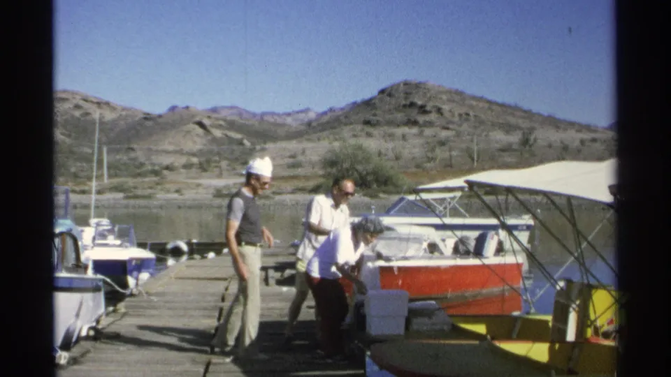 The older woman bends near the docked boat while two men remain close by on the Guaymas marina dock in 1975.