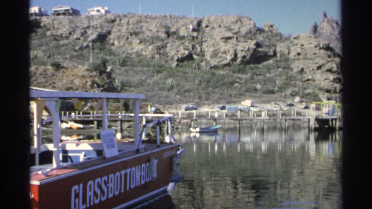 Red glass-bottom boat at a marina with rocky hills behind calm water.