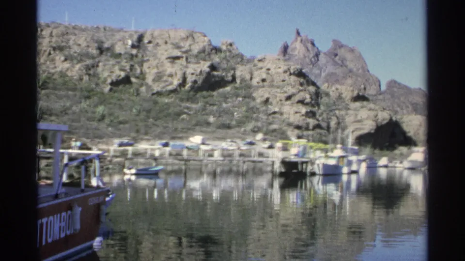 1975 Guaymas footage pans across calm marina water, docked boats, rocky desert slopes, and the edge of a red glass-bottom boat.