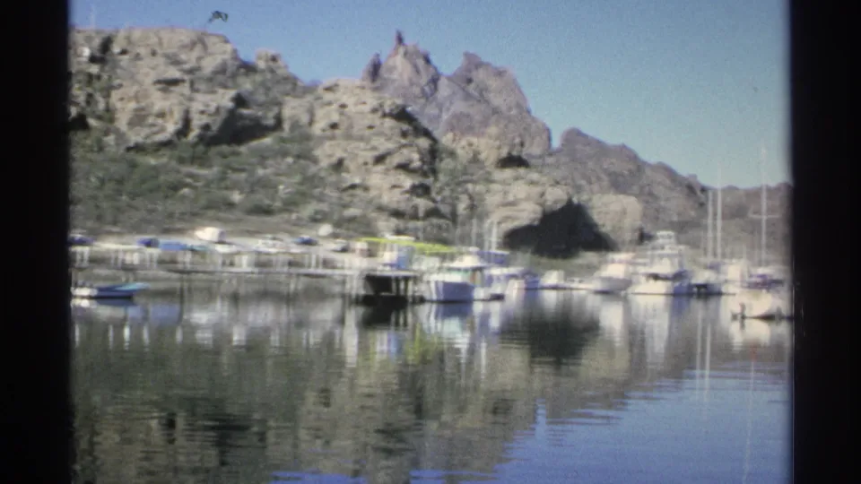 1975 Guaymas marina view with small boats, still reflections, and rugged desert mountains behind the docks.