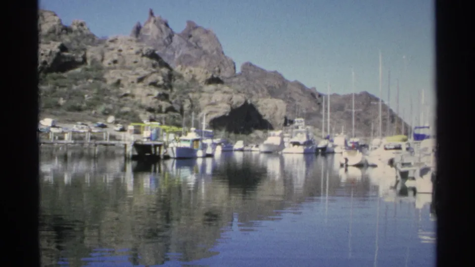 Guaymas, Mexico marina scene with sailboat masts, motorboats, docks, and desert mountains under a clear sky.