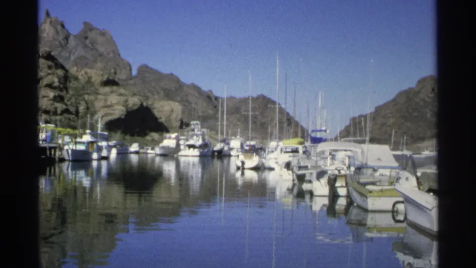 Guaymas marina view with small boats along docks, tall masts, calm blue water, and desert mountains beyond.