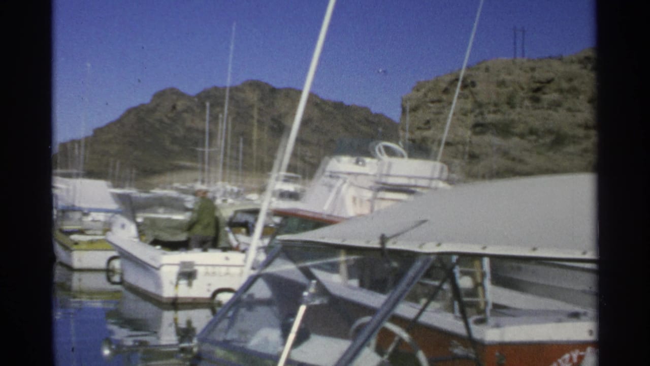 Docked boats and masts in a marina with rocky desert hills behind them.