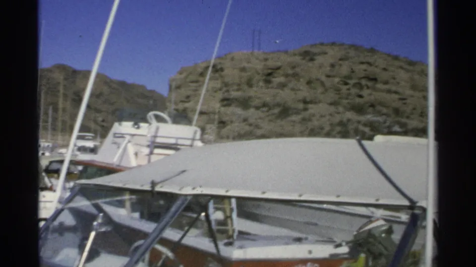 1975 Guaymas marina frame showing canvas-covered boats, masts, docked vessels, and rugged hills under a clear sky.