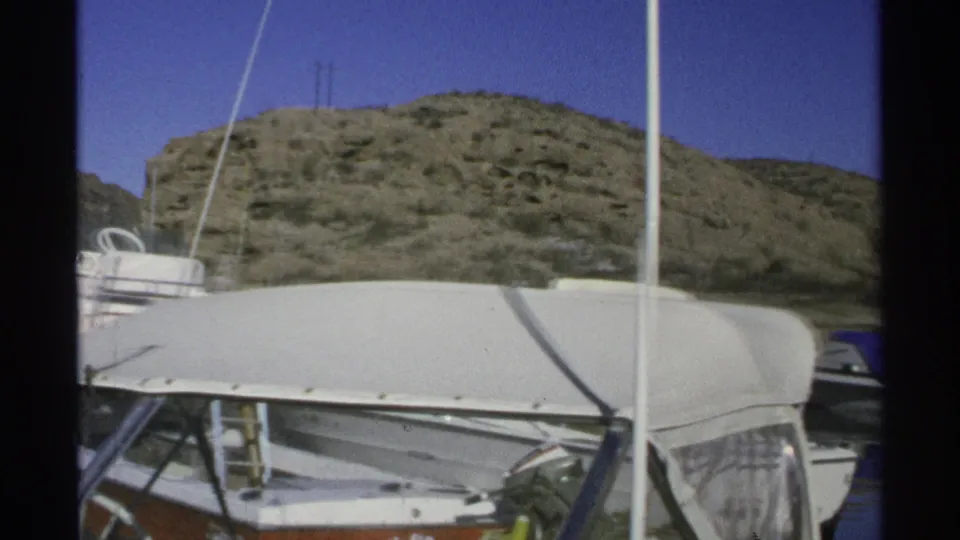 1975 Guaymas marina detail with a boat canopy and vertical mast in front of a scrub-covered desert hillside.