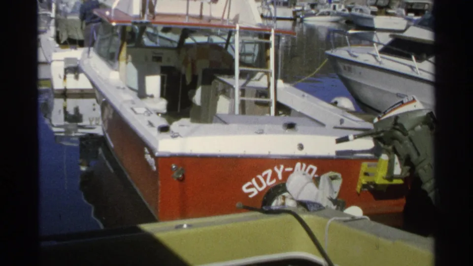 1975 Guaymas marina frame with the red-and-white vessel SUZY-NO docked near other small boats and outboard motors.