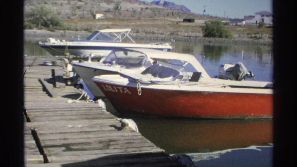 1975 Guaymas marina frame showing the red boat LOLITA moored beside a wooden dock and still water.