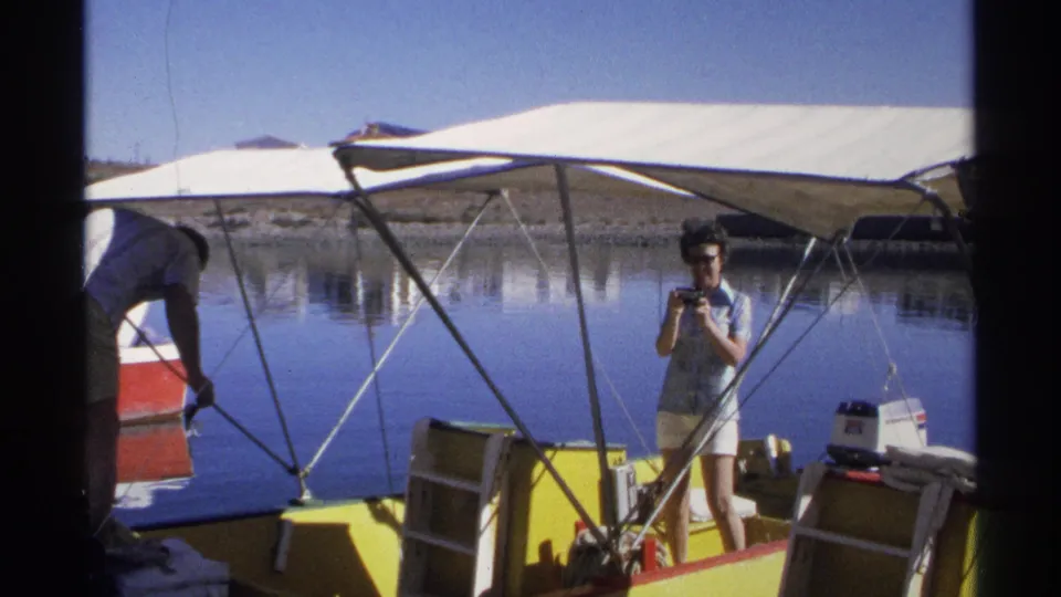 A woman appears to take a photograph from the yellow boat as a man bends near the neighboring red boat on calm water in Guaymas.