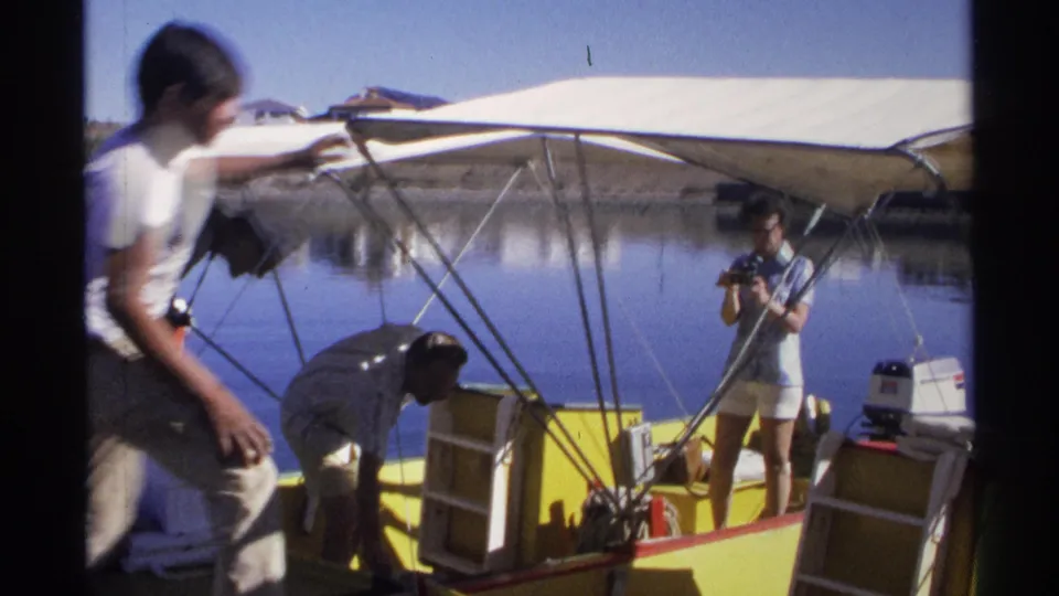 Two men work around the yellow boat while the woman stands with a camera, showing informal 1975 vacation boat preparation in Guaymas.