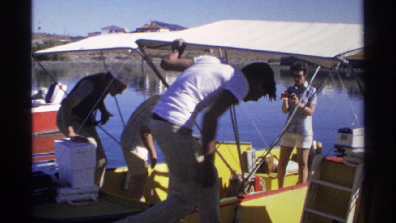 In Guaymas, Mexico, 1975 home-movie footage, adults load coolers and adjust gear on a yellow motorboat under a white canopy.
