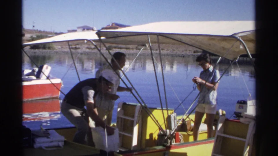 Adults finish arranging gear on a yellow motorboat in Guaymas, Mexico, with a woman filming near calm water in the background.