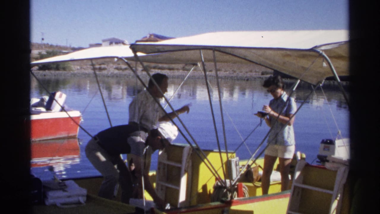 In Guaymas, Mexico, 1975 home-movie footage, three people prepare on a yellow and white motorboat with a canvas canopy.