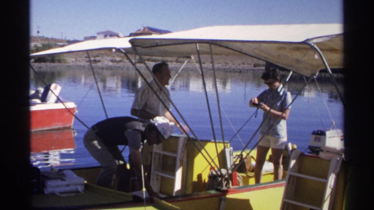 People stand and bend over inside a small motorboat near still water.