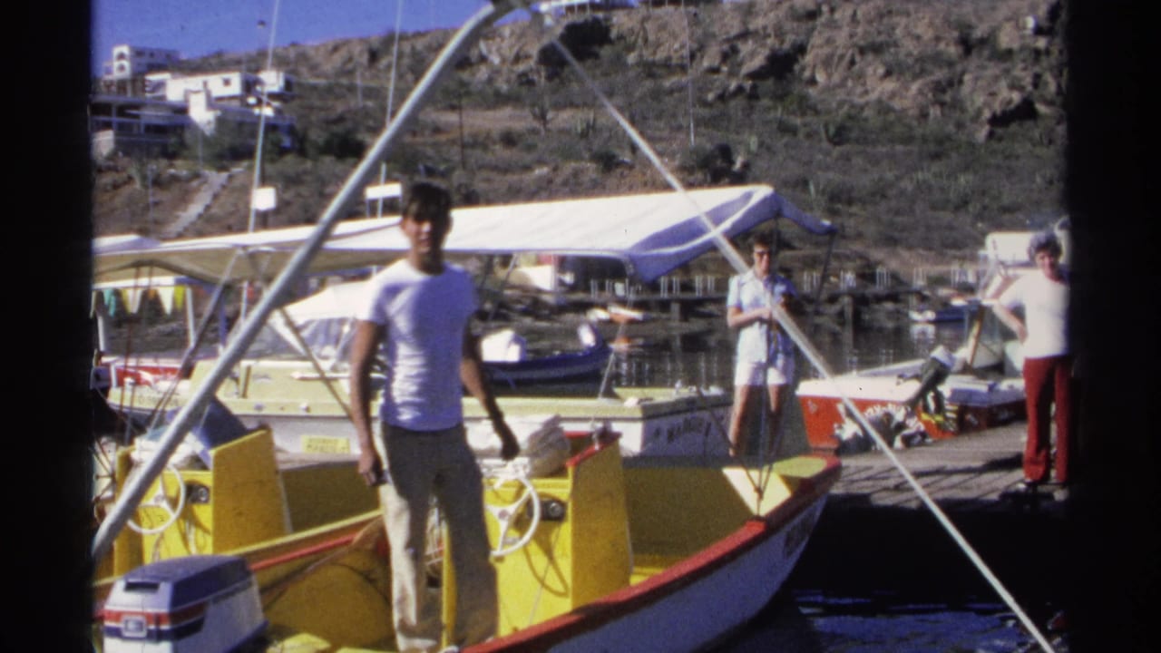 Man on yellow motorboat with docked boats and people behind him.
