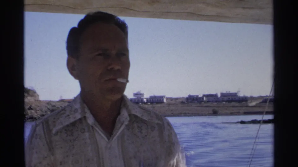 In 1975 Guaymas, Mexico footage, a man in a patterned shirt holds a cigarette in his mouth aboard a small moving boat.