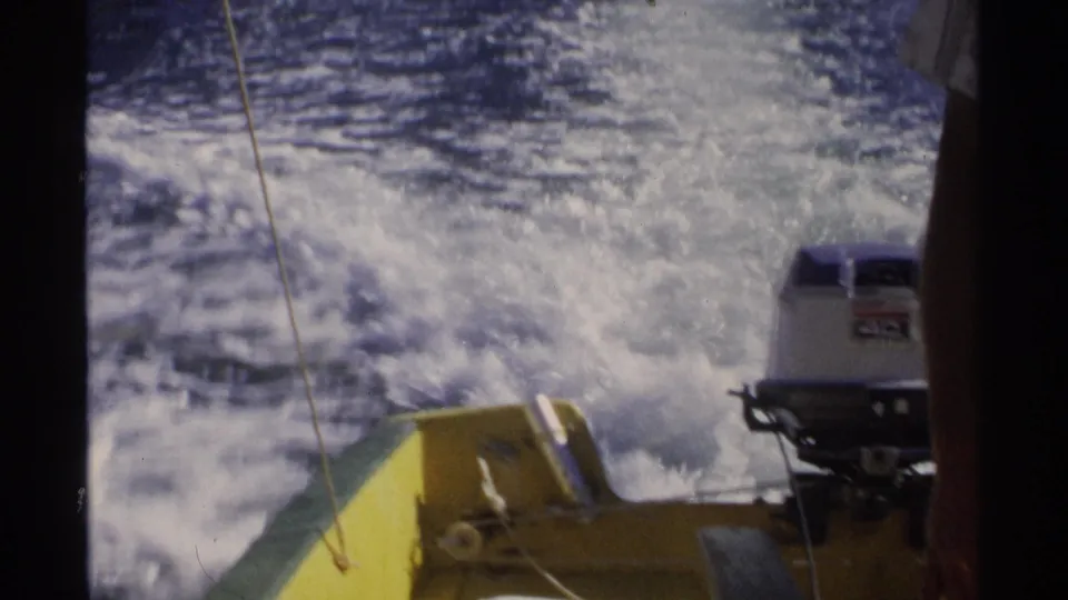 The stern of the speedboat shows churning wake, yellow boat structure, a cord, and an outboard motor with a visible marking.