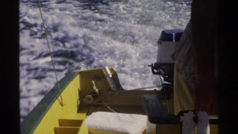 1975 Guaymas home-movie frame looking past a yellow boat stern and labeled outboard motor toward churning water.