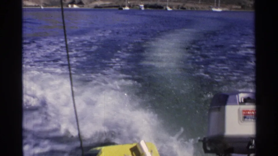 1975 Guaymas home-movie frame showing the wake spreading behind a moving boat, with distant shoreline boats near the horizon.