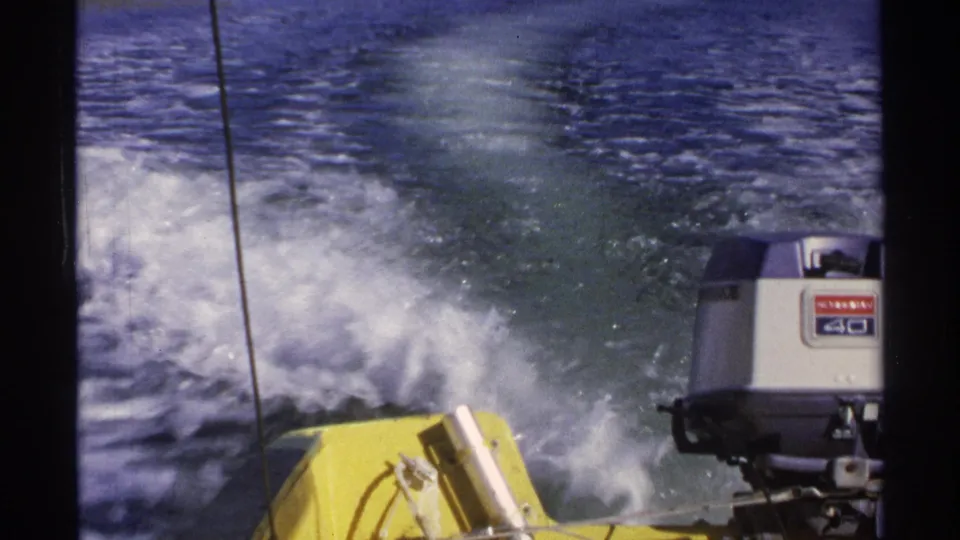 Rear-facing 1975 Guaymas frame with the yellow boat corner, labeled outboard motor, vertical cable, and white spray behind.