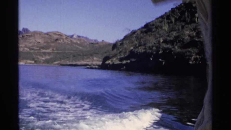 Guaymas coastal boating frame from 1975, with the speedboat wake leading toward open water and a rocky headland at right.