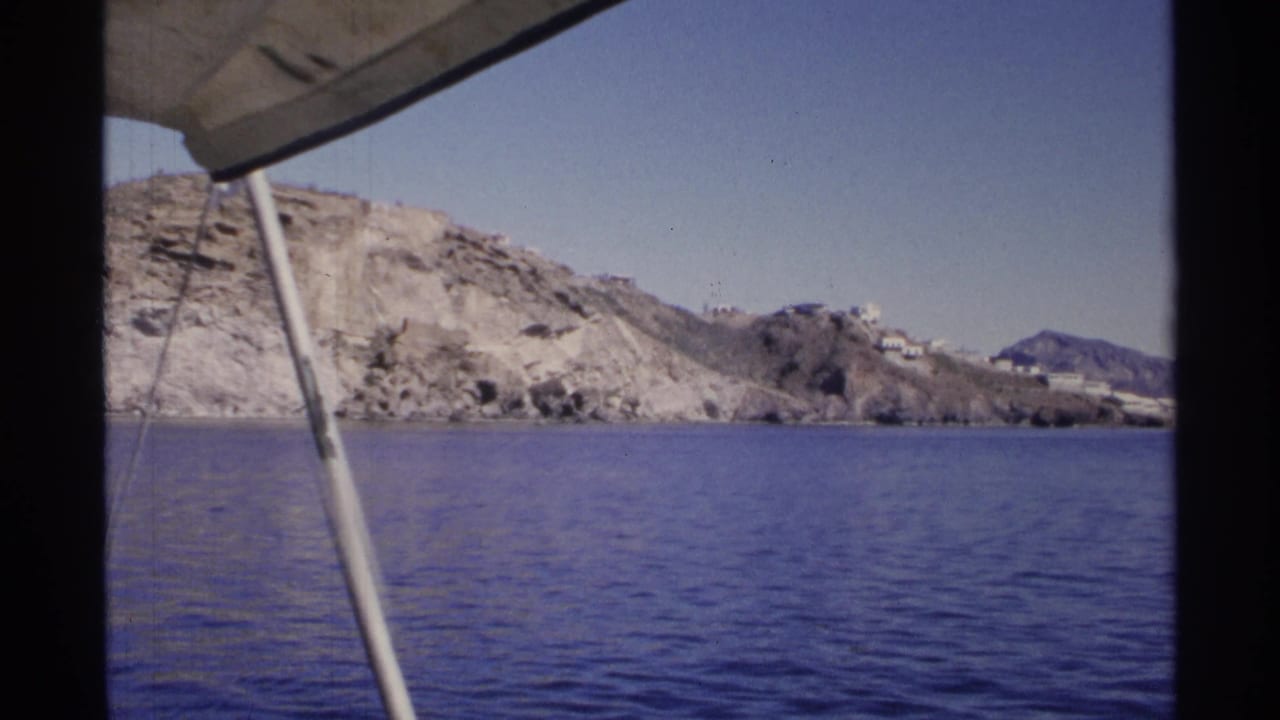 Rocky shoreline and blue sea framed by a boat support pole and canopy.