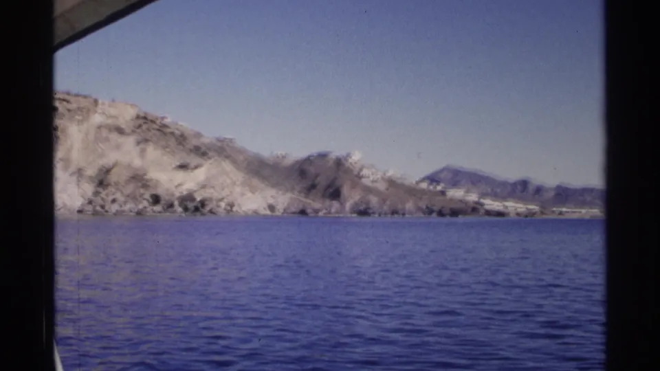 Guaymas coastal view from the boat, showing calm water, pale rocky cliffs, and hazy mountains under a clear sky.