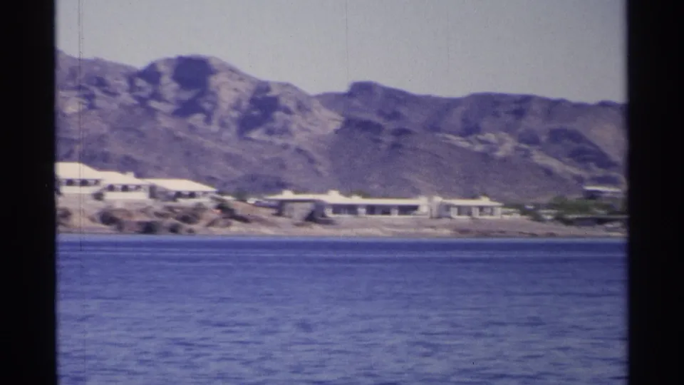 Guaymas, Mexico 1975 frame showing a low shoreline complex against rugged mountains, seen across blue water.