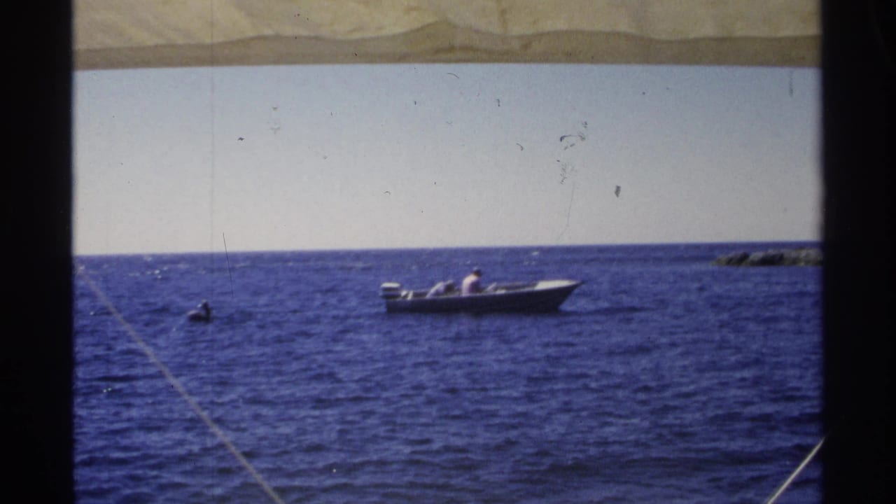 1975 Guaymas, Mexico 8mm frame showing a small motorboat offshore, framed by a shaded canvas awning and open sea.