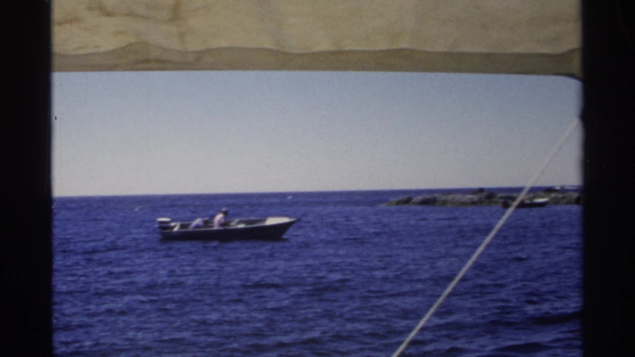 Motorboat crossing blue water with low rocks in the distance.