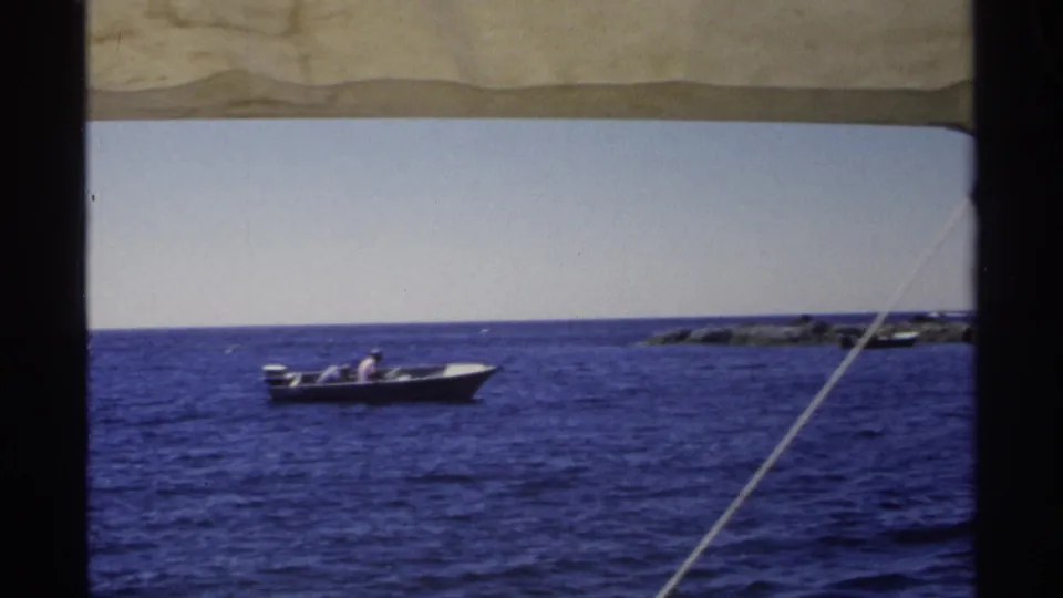 1975 Guaymas, Mexico frame of a small motorboat passing over vivid blue water near distant rocky shoreline.