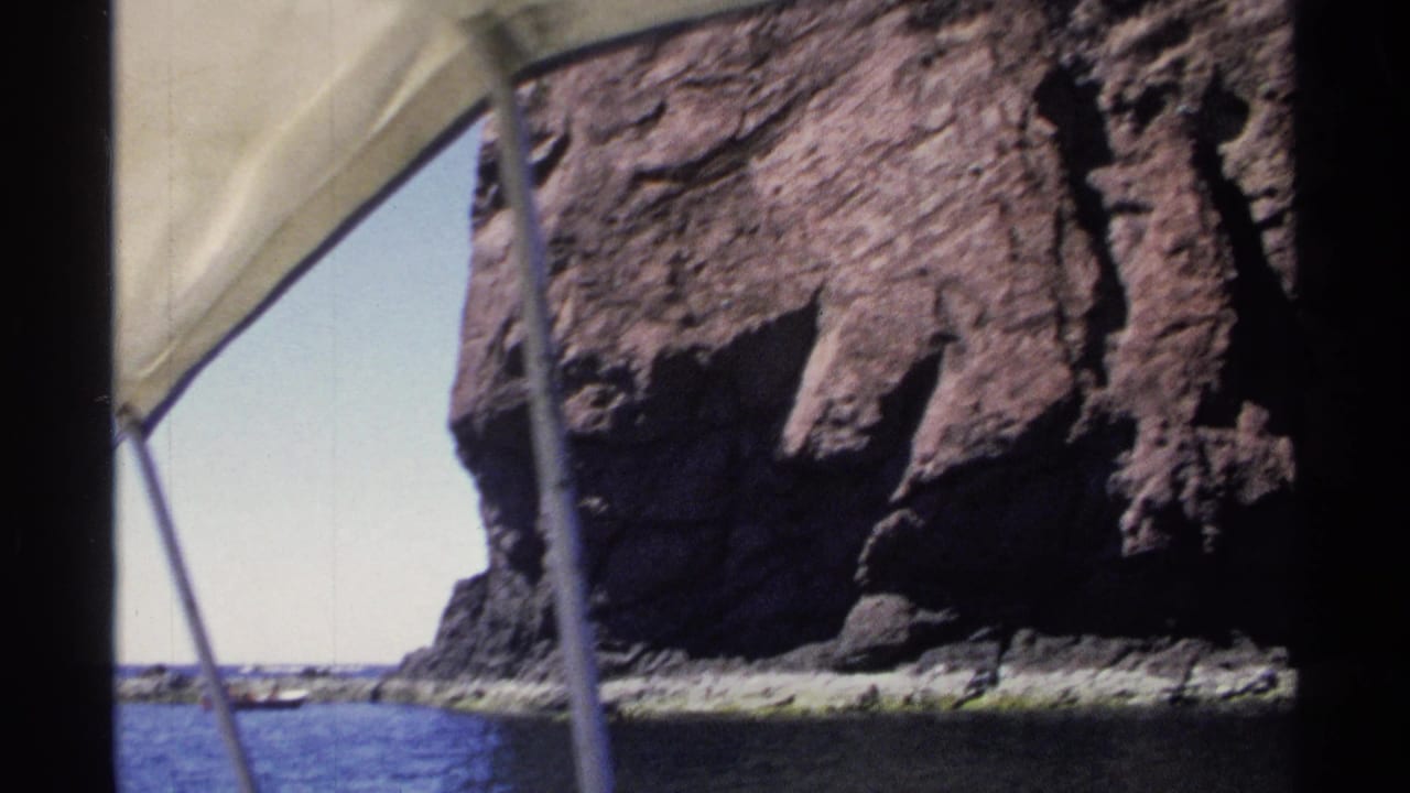 Rocky sea cliff viewed from a boat with canopy fabric and support poles visible.