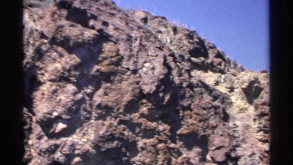 Close 1975 8mm view of rugged Guaymas boulders and jagged cliff texture beneath a clear blue sky.