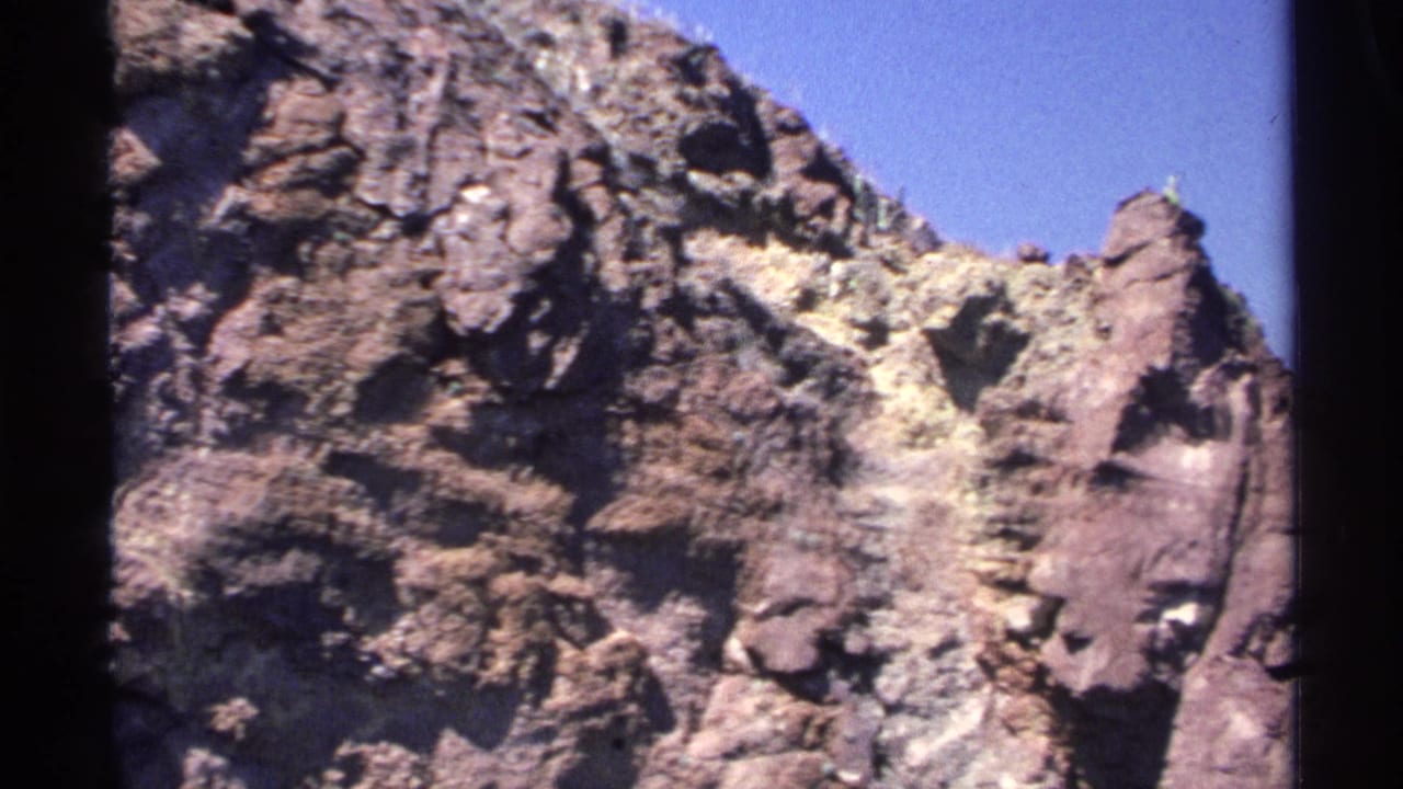 1975 8mm Guaymas footage showing a rugged coastal rock face beneath clear blue sky with visible film-frame borders.