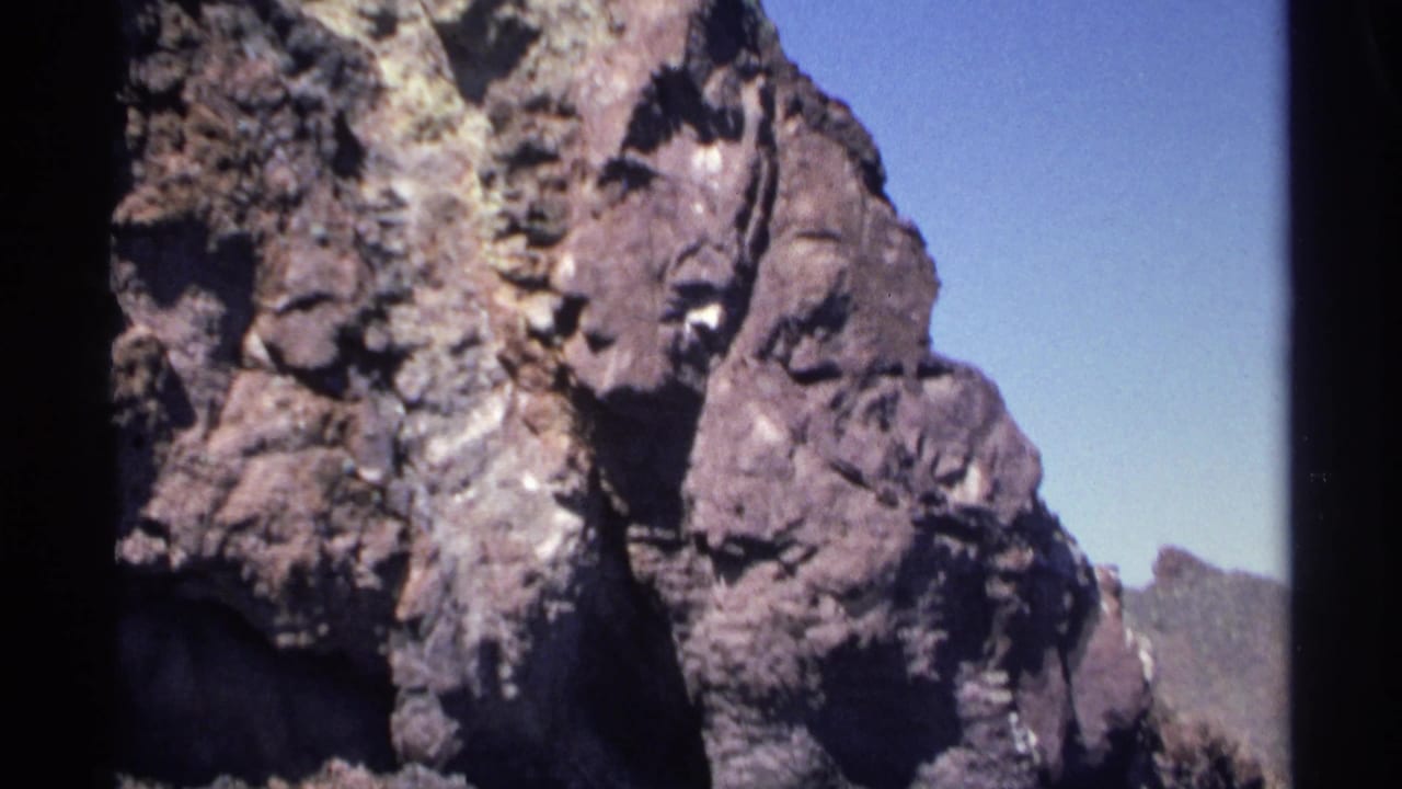 Close coastal cliff face with jagged rock texture and blue sky.